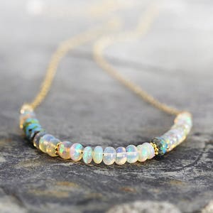 May include: A delicate gold chain necklace with a row of white opal beads and two blue and green accent beads.