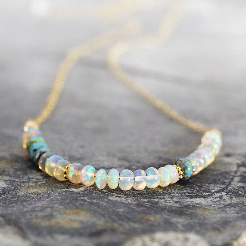 May include: A delicate gold chain necklace with a row of white opal beads and two blue and green accent beads.