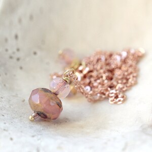 May include: A delicate necklace featuring a cluster of pink and gold beads. The focal point is a faceted, mauve-colored bead, complemented by smaller, translucent pink beads. The necklace has a fine, rose-gold chain.