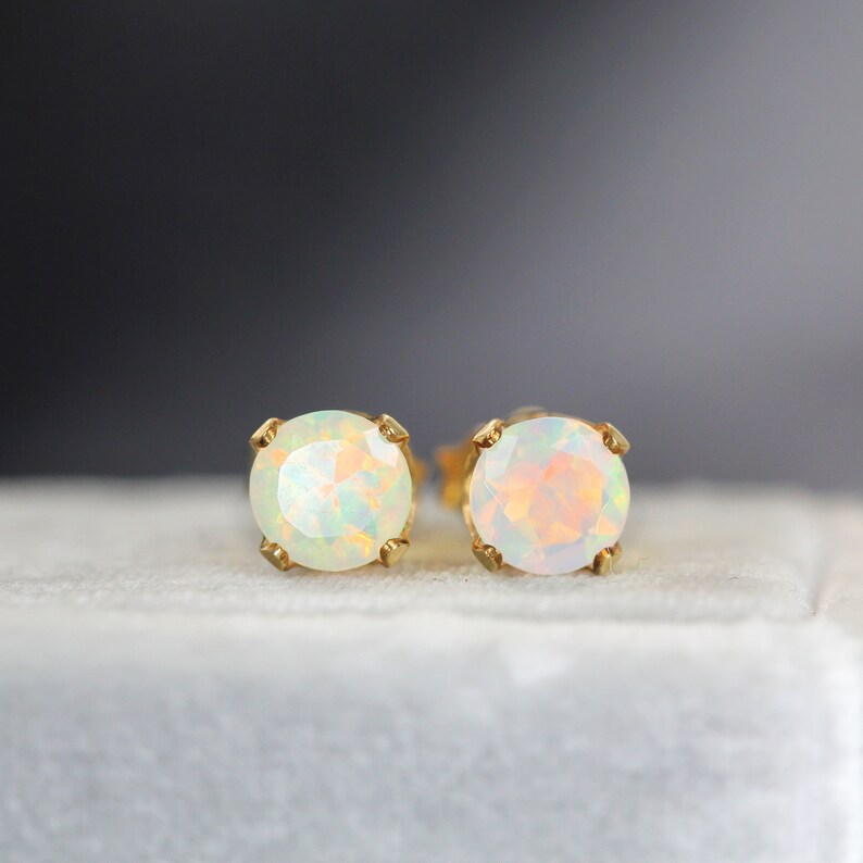 May include: A pair of gold stud earrings with white opal gemstones. The earrings are set in a simple, classic style.