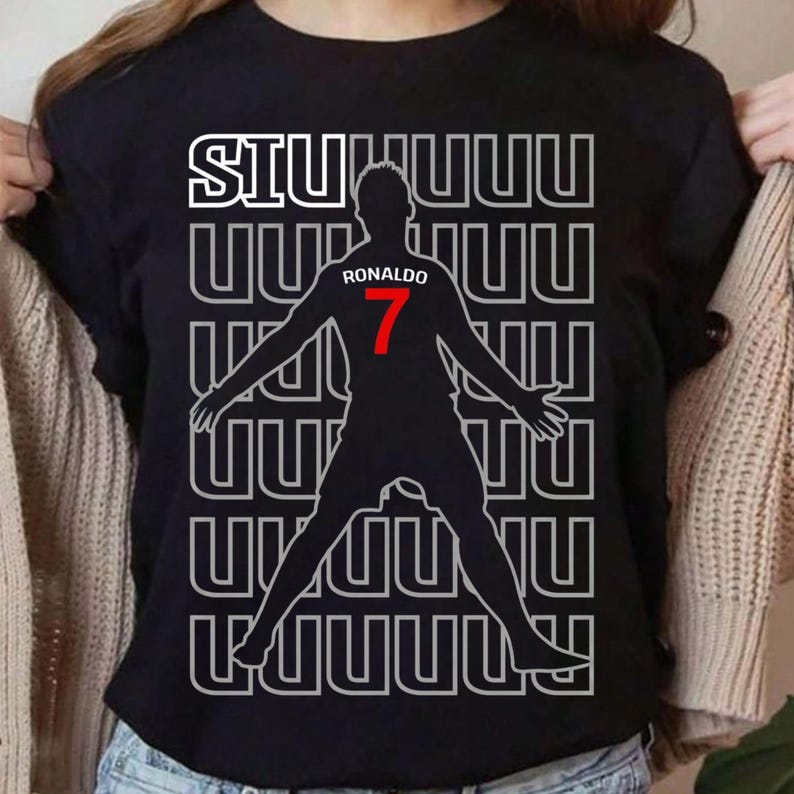 May include: Black t-shirt featuring a silhouette of a soccer player with outstretched arms. The shirt has the word "SIUUUU" in white block letters at the top, with the name "Ronaldo" and the number "7" in red.