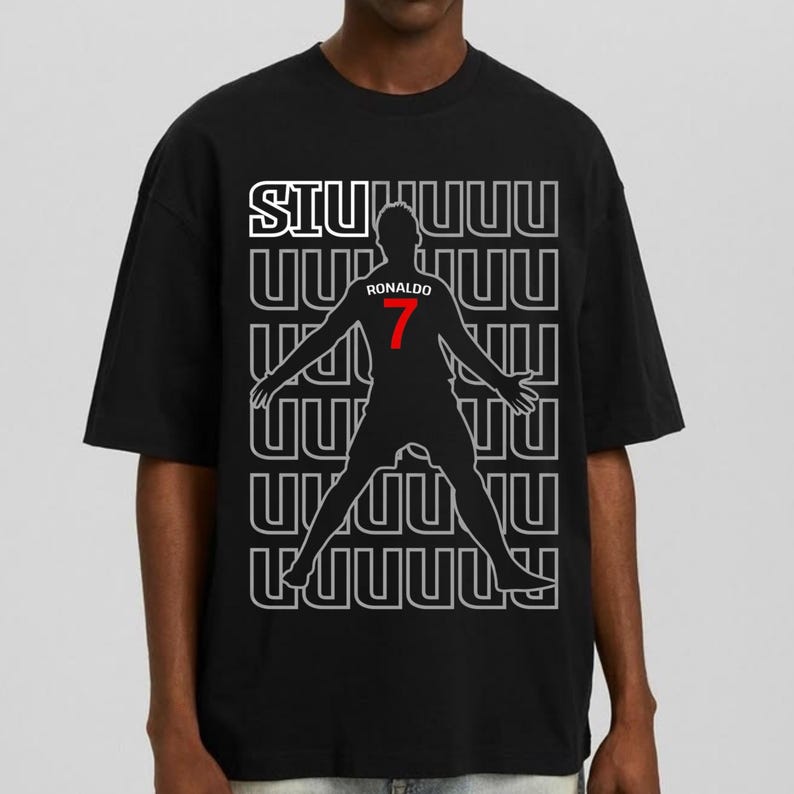 May include: Black t-shirt featuring a silhouette of a soccer player with the number 7 in red. The shirt has the word "SIU" in white and the player's name "Ronaldo" above the number. The background has a repeating pattern.