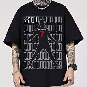 May include: Black t-shirt featuring a silhouette of a soccer player with outstretched arms. The shirt has the word "SIU" in white, the name "RONALDO" and the number "7" in red. The background has a repeating pattern of the letter "U".