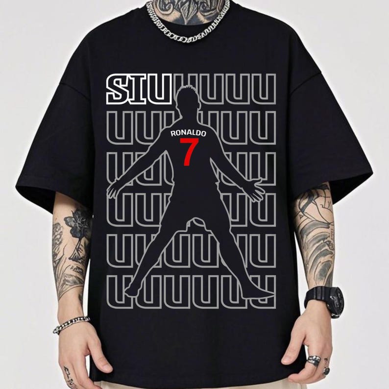 May include: Black t-shirt featuring a silhouette of a soccer player with outstretched arms. The shirt has the word "SIU" in white, the name "RONALDO" and the number "7" in red. The background has a repeating pattern of the letter "U".
