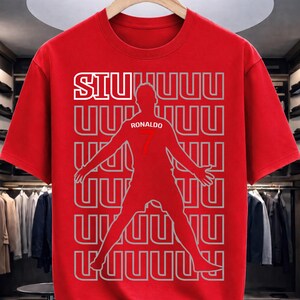 May include: Red t-shirt featuring a silhouette of a soccer player with outstretched arms. The shirt has the word "SIU" in white block letters at the top, and the name "Ronaldo" and the number "7" are visible on the player's jersey.
