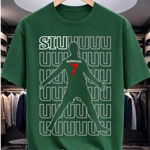 May include: Green t-shirt featuring a silhouette of a soccer player with the name "Ronaldo" and the number "7" in red. The shirt also has the word "SIU" in white, with a repeating pattern of the letter "U".