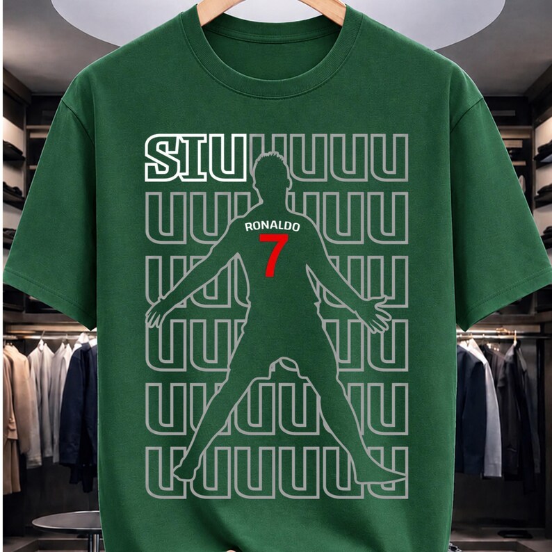 May include: Green t-shirt featuring a silhouette of a soccer player with the name "Ronaldo" and the number "7" in red. The shirt also has the word "SIU" in white, with a repeating pattern of the letter "U".