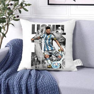 May include: White square throw pillow featuring a graphic of a soccer player in a blue and white striped jersey kicking a soccer ball. The pillow has the name "Lionel Messi" in large black letters.