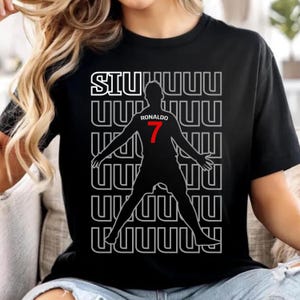 May include: Black t-shirt featuring a silhouette of a soccer player with the number 7 in red. The shirt has the word "SIUUUU" in white above the silhouette and the name "RONALDO" in white above the number 7.