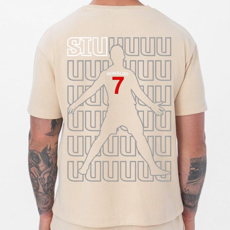 May include: Beige t-shirt featuring a silhouette of a soccer player with outstretched arms. The number 7 is in red, and the name "Ronaldo" is above it. The word "SIUUUU" is at the top in white.