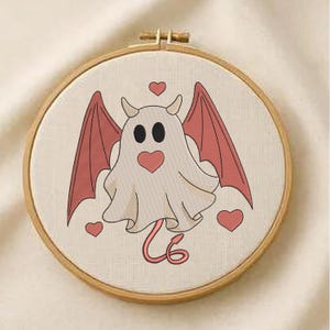 Può includere: Un telaio da ricamo stravagante con un design di fantasma diabolico. Il fantasma è bianco con ali, corna e una coda a forma di cuore rosse. Ulteriori cuori rossi sono sparsi intorno al disegno, su un tessuto color crema.