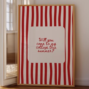 May include: A framed art print featuring a red and white striped background with the text "Will you come to my cottage this summer?" in a red, cursive font. The artwork is displayed in a room with natural light.