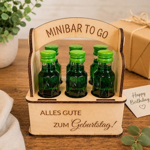 May include: A wooden carrier with a handle inscribed MINIBAR TO GO and ALLES GUTE ZUM GEBURTSTAG, holding six small green glass bottles with bright green screw caps. The carrier is made from light-coloured plywood with dark brown edges.