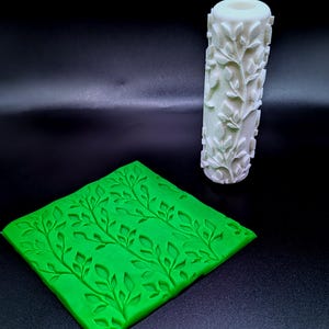 May include: A white rolling pin with a leaf and vine pattern, alongside a bright green square mold featuring a similar leaf and vine design. These items are likely for baking or crafting purposes.