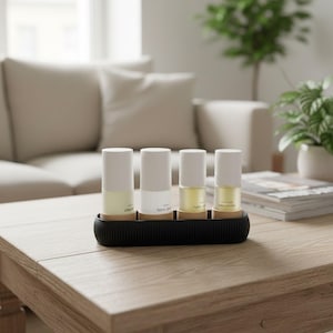 Könnte beinhalten: Vier zylindrische Flaschen mit weißen Deckeln und klaren Glasböden, die jeweils eine unterschiedlich farbige Flüssigkeit enthalten, sind in einem schwarzen Tablett angeordnet. Die Flaschen sind mit den Wörtern "Clean", "Tonic" und "Soothing" beschriftet.