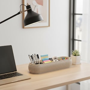 Könnte beinhalten: Ein beiger Schreibtisch-Organizer mit Stiften, Haftnotizen, Büroklammern und Reißzwecken steht auf einem Holzschreibtisch. Ein Laptop und eine schwarze Schreibtischlampe sind ebenfalls vorhanden. Rechts befindet sich eine kleine Topf-Sukkulente.