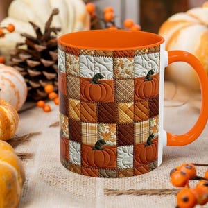 Peut inclure: Un mug en céramique avec un intérieur et une anse orange vif, présentant un motif extérieur de patchwork matelassé. Le design se compose de carrés alternés dans des tons de marron, crème et orange, décorés avec des motifs de citrouilles.