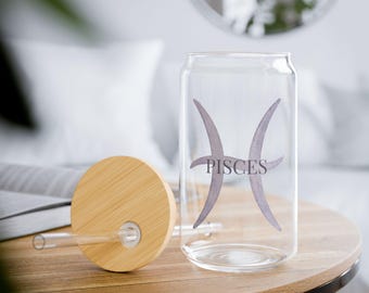 May include: A clear glass can-shaped tumbler with a bamboo lid and straw. The tumbler features a purple Pisces zodiac symbol and the word "PISCES". The lid is round and made of light-colored bamboo.