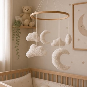 Puede incluir: Un móvil colgante para habitación infantil con un marco circular de madera suspendido por hilos blancos. Incluye varias nubes y lunas crecientes blancas de felpa texturizada, hechas de un material suave y esponjoso.