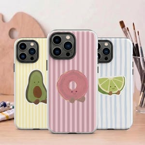 Könnte beinhalten: Drei Smartphone-Hüllen mit vertikalen Streifen und niedlichen Charakter-Illustrationen. Die linke Hülle ist gelb mit einer Avocado, die mittlere Hülle ist rosa mit einem Donut und die rechte Hülle ist hellblau mit einer Limettenscheibe.