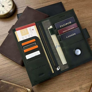May include: Open dark green leather travel wallet with multiple card slots, a zippered compartment, and a snap closure. The wallet contains a passport, cards, and a boarding pass. The text "YOU ARE MY HERO" is visible on the wallet.
