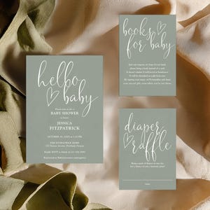 Puede incluir: Tarjetas de invitación a baby shower verde salvia con texto en escritura blanca. Las tarjetas incluyen texto que dice "hello baby", "books for baby" y "diaper raffle". Las tarjetas están dispuestas sobre un fondo de tela beige.