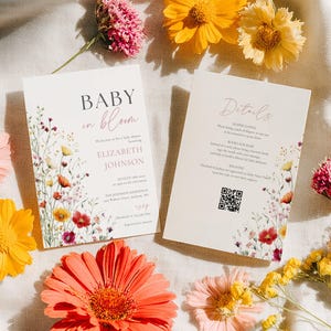 May include: Two baby shower invitations with floral designs and the text "Baby in Bloom" and "Details". The invitations are surrounded by colorful flowers in shades of pink, orange, and yellow, creating a cheerful and inviting aesthetic.