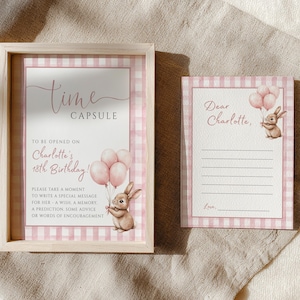 Puede incluir: Un letrero enmarcado de "Cápsula del tiempo" y una tarjeta a juego. El letrero tiene un borde rosa a cuadros y el texto "Cápsula del tiempo" y "¡Para abrir en el 18 cumpleaños de Charlotte!" Un conejito de acuarela sostiene globos. La tarjeta dice "Querida Charlotte".