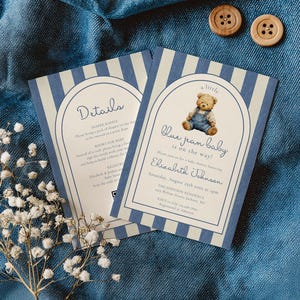 Könnte beinhalten: Zwei Babyparty-Einladungen mit blau-weißem Streifenmuster. Die Einladungen zeigen den Text "Blue Jean Baby is on the way!" und enthalten eine Teddybär-Illustration. Der Hintergrund ist ein blauer Stoff.