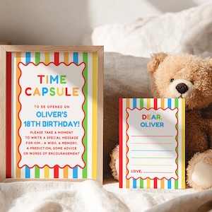 May include: A framed "Time Capsule" sign and a matching card with a teddy bear. The sign has colorful vertical stripes and text that reads "Time Capsule" and "Oliver's 18th Birthday!" The card says "Dear, Oliver" and has lines for writing.