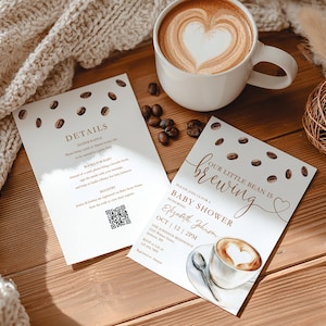 May include: Two baby shower invitations with coffee bean illustrations and the text "Our little bean is brewing." A cup of coffee with latte art and coffee beans are also visible. The invitations are on a wooden surface.