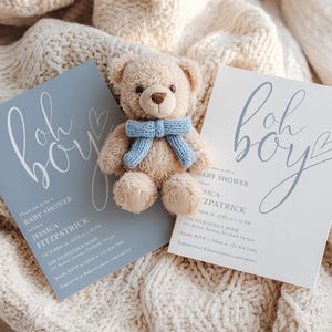 May include: Baby shower invitations with the words "Oh Boy" in cursive script, a small teddy bear with a blue scarf, and a light blue invitation card. The invitation includes details for Jessica Fitzpatrick's baby shower.