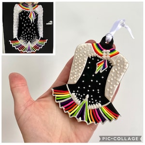 May include: Ornament shaped like an Irish dance dress. The black dress has white polka dots and a rainbow-colored trim. The shoulders are white with small white dots. A rainbow design is at the neckline and a white ribbon is attached.