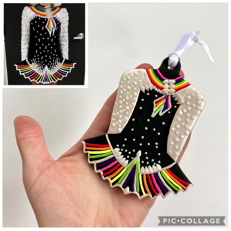 May include: Ornament shaped like an Irish dance dress. The black dress has white polka dots and a rainbow-colored trim. The shoulders are white with small white dots. A rainbow design is at the neckline and a white ribbon is attached.