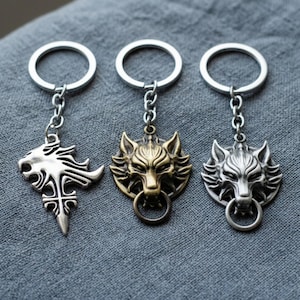 Peut inclure: Trois porte-clés en métal avec des motifs de loup et de lion. Un porte-clés présente un emblème de lion argenté, tandis que les deux autres présentent des têtes de loup en bronze et en argent. Chaque porte-clés a un anneau pour les clés.