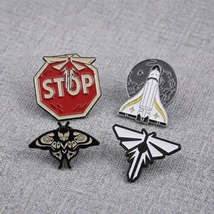 May include: Four enamel pins featuring a red octagonal stop sign with a firefly symbol, a white space shuttle against a grey moon, a black and cream moth with intricate wing patterns, and a black and white stylized firefly symbol with sharp wings.