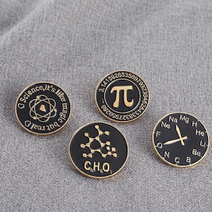 Puede incluir: Cuatro pines de esmalte negro y dorado con temática científica. Un pin presenta un símbolo de átomo con el texto "Science, it's like magic but real". Otro muestra el símbolo Pi con números. El tercero muestra una estructura química, y el cuarto tiene un diseño de reloj con símbolos de elementos.