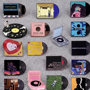 Puede incluir: Una colección de pines de esmalte con forma de discos de vinilo y portadas de álbumes. Los pines presentan varias ilustraciones coloridas, texto que incluye 'Music Please', 'Divide', 'Cigarettes After Sex' y 'Wanna See My Records', y tocadiscos en miniatura.