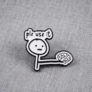 May include: A black and white enamel pin featuring a stick figure character with a blank expression. The character holds a brain in one hand, and a speech bubble above its head contains the black text "plz use it" in a casual, handwritten font.