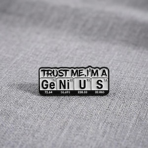 May include: A rectangular black and white enamel pin featuring the text TRUST ME, I'M A at the top. Below, the word GENIUS is styled like periodic table elements with atomic numbers 32, 28, 92, 16 and atomic weights 72.64, 58.693, 238.03, 32.065.