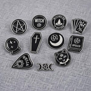 May include: A selection of black and silver enamel pins with witchy and occult designs. The pins feature a pentagram, a coffin, a crystal ball, a cat, a Ouija planchette, playing cards, and the text "Witch" and "Witches do it better".