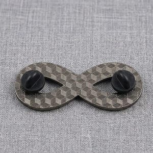 Pu&ograve; includere: Una spilla in metallo a forma di simbolo dell'infinito con un motivo geometrico a cubi testurizzati sulla superficie. Il retro della spilla presenta due chiusure in gomma nera, utilizzate per fissare l'accessorio al tessuto o ad altri materiali.