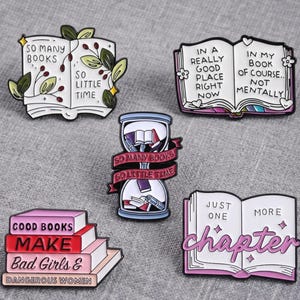 May include: Five enamel pins featuring book themes. One shows an open book with leaves and text "SO MANY BOOKS SO LITTLE TIME". Another is an open book with text "IN A REALLY GOOD PLACE RIGHT NOW IN MY BOOK OF COURSE.. NOT MENTALLY". An hourglass pin with books inside and a banner reading "SO MANY BOOKS SO LITTLE TIME". A stack of four books with text "GOOD BOOKS MAKE BAD GIRLS & DANGEROUS WOMEN". An open book with text "JUST ONE MORE chapter".