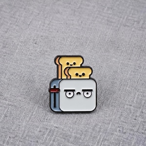 May include: A metal enamel pin shaped like a white toaster with a grumpy face, featuring two slices of light yellow toast with happy faces popping out of the top. The toaster has a small red lever on the side and black outlines throughout the design.