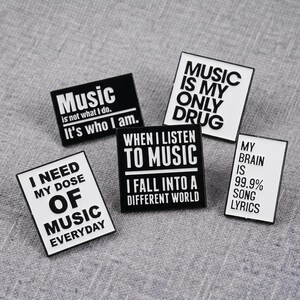 Könnte beinhalten: Fünf rechteckige Emaille-Anstecknadeln mit schwarz-weißen Designs und musikbezogenem Text. Die Anstecknadeln zeigen Sätze wie Music is not what I do, It's who I am, Music is my only drug, I need my dose of music everyday und My brain is 99.9% song lyrics.