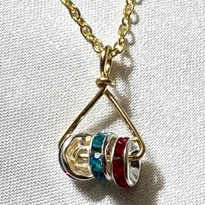 May include: A gold-colored necklace with a pendant featuring a silver-colored charm and three rings with blue and red gemstones. The necklace has a delicate chain and a triangular pendant design.