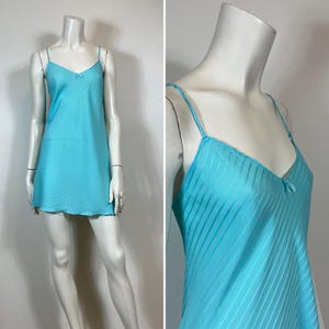 K&ouml;nnte beinhalten: Ein hellblaues Satin-Schlafkleid mit d&uuml;nnen Tr&auml;gern und einer zarten Schleife am Ausschnitt. Das Kleid hat ein gestreiftes Muster.