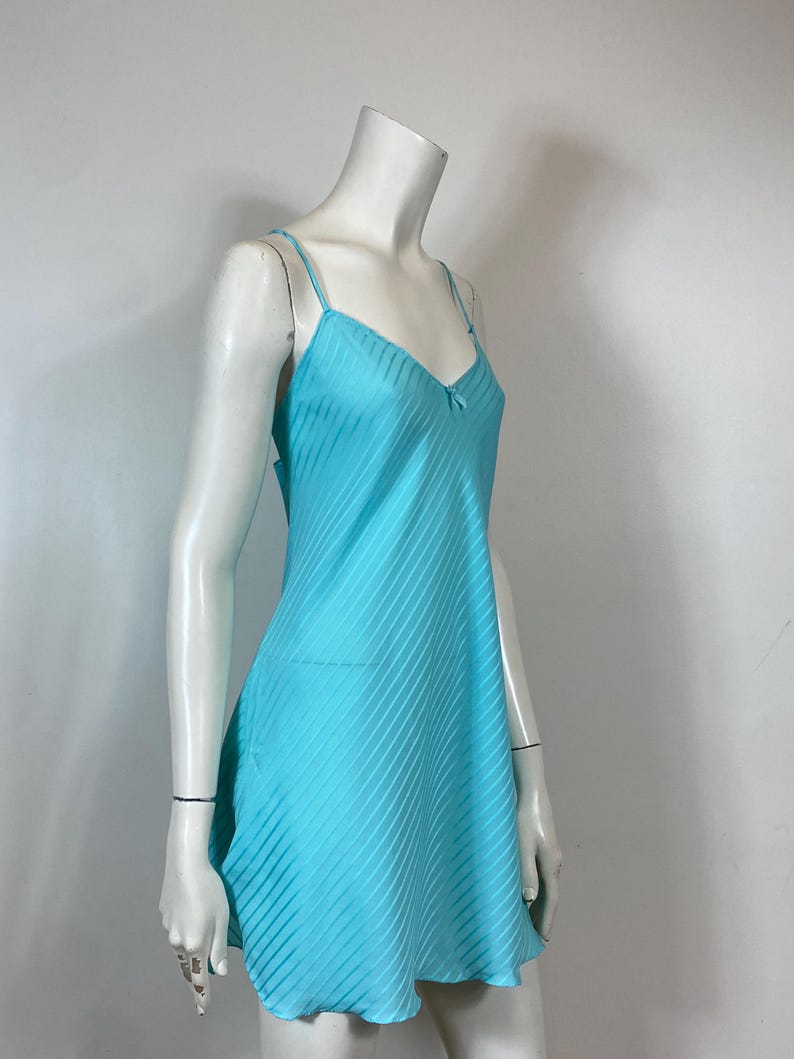 K&ouml;nnte beinhalten: Ein hellblaues Satin-Schlafkleid mit d&uuml;nnen Tr&auml;gern und einer zarten Schleife am Ausschnitt.
