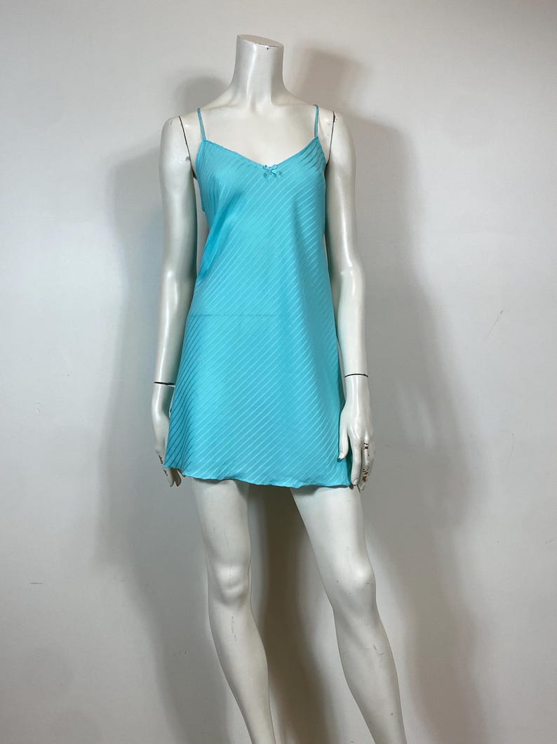 K&ouml;nnte beinhalten: Ein hellblaues, &auml;rmelloses Schlupfkleid mit einem d&uuml;nnen wei&szlig;en Streifenmuster. Das Kleid hat einen V-Ausschnitt und eine Schleife am Ausschnitt.