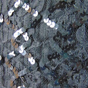 May include: Close-up of a black fabric with silver sequins arranged in a geometric pattern.